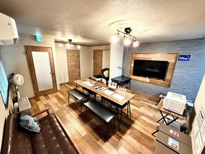 Una stanza con pavimento in legno, un tavolo da pranzo con panche, una TV a parete e una ventola a soffitto.