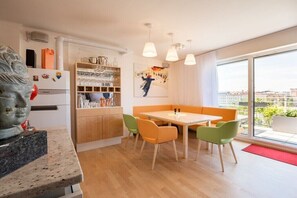 Une cuisine moderne dotée d’un réfrigérateur encastré, un coin repas avec une table et des chaises, et une grande fenêtre offrant une vue sur la ville.