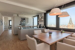 A modern kitchen with a central island, a dining area with a wooden table, and large windows offering a city view. - Skyflats Vienna City View (Wien)