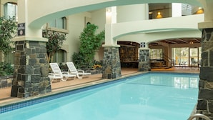 An indoor swimming pool with stone pillars, lounge chairs, and a view of the interior. - Family Loft Suite in Banff w/ Rocky Mountain Views (Banff)