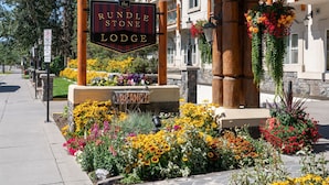 A sign for the Rundle Stone Lodge with a 'VACANCY' sign below it, surrounded by a flower bed. - Family Loft Suite in Banff w/ Rocky Mountain Views (Banff)