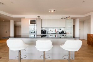 A modern kitchen with a central island, white bar stools, and stainless steel appliances. - Skyflats Vienna South View (Wien)