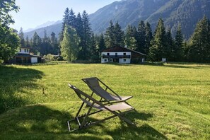 Ein grünes Feld mit einem Liegestuhl, einem Holzhaus und einem Berg im Hintergrund.