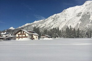 Eine verschneite Berglandschaft mit einem Chalet mit mehreren Balkonen und einer Skipiste im Vordergrund.