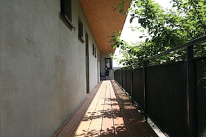 A narrow corridor with a wooden deck, a black metal fence, and a building with a textured ceiling. - 1 - Langerwisch Manor (Michendorf OT Langerwisch)