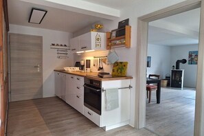 Eine kompakte Küche mit weißen Schränken, einer Holz Arbeitsplatte und einem kleinen Backofen. Im Hintergrund ist ein Essbereich mit Tisch und Stühlen zu sehen.