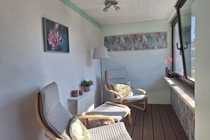 Ein Balkon mit zwei Stühlen, einer Stehlampe, einem Wandbild und einem Fenster mit Blick.