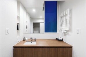 Uma casa de banho moderna com toucador de madeira, uma pia branca, um espelho e uma parede de destaque azul.