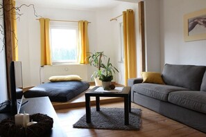 Ein Wohnzimmer mit Sofa, Couchtisch, Pflanze und einem Vorhangfenster.