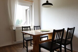 Ein Essbereich mit Tisch und Stühlen, einem Fenster mit Vorhängen, einem Heizkörper und einer Hängelampe.