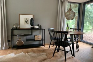 A dining area with a round table, black chairs, a black bookshelf, and a hanging light fixture. - Bungalow in the forest (Borkwalde)