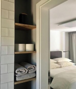 A hotel room with a bed, a nightstand, a lamp, and a shelf with towels and a container. - Bungalow in the forest (Borkwalde)