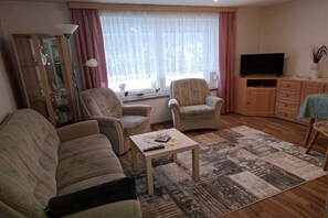Ett vardagsrum med en soffa, två fåtöljer, ett soffbord, en tv och ett skåp.