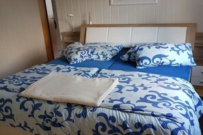 Ein Bett mit einer blau-weißen Bettdecke, zwei passende Kissen und einer beigen Tagesdecke.