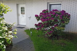 Ein weißes Backsteingebäude mit einer weißen Tür, einem kleinen Fenster und einem Blumentopf mit violetten Blüten.