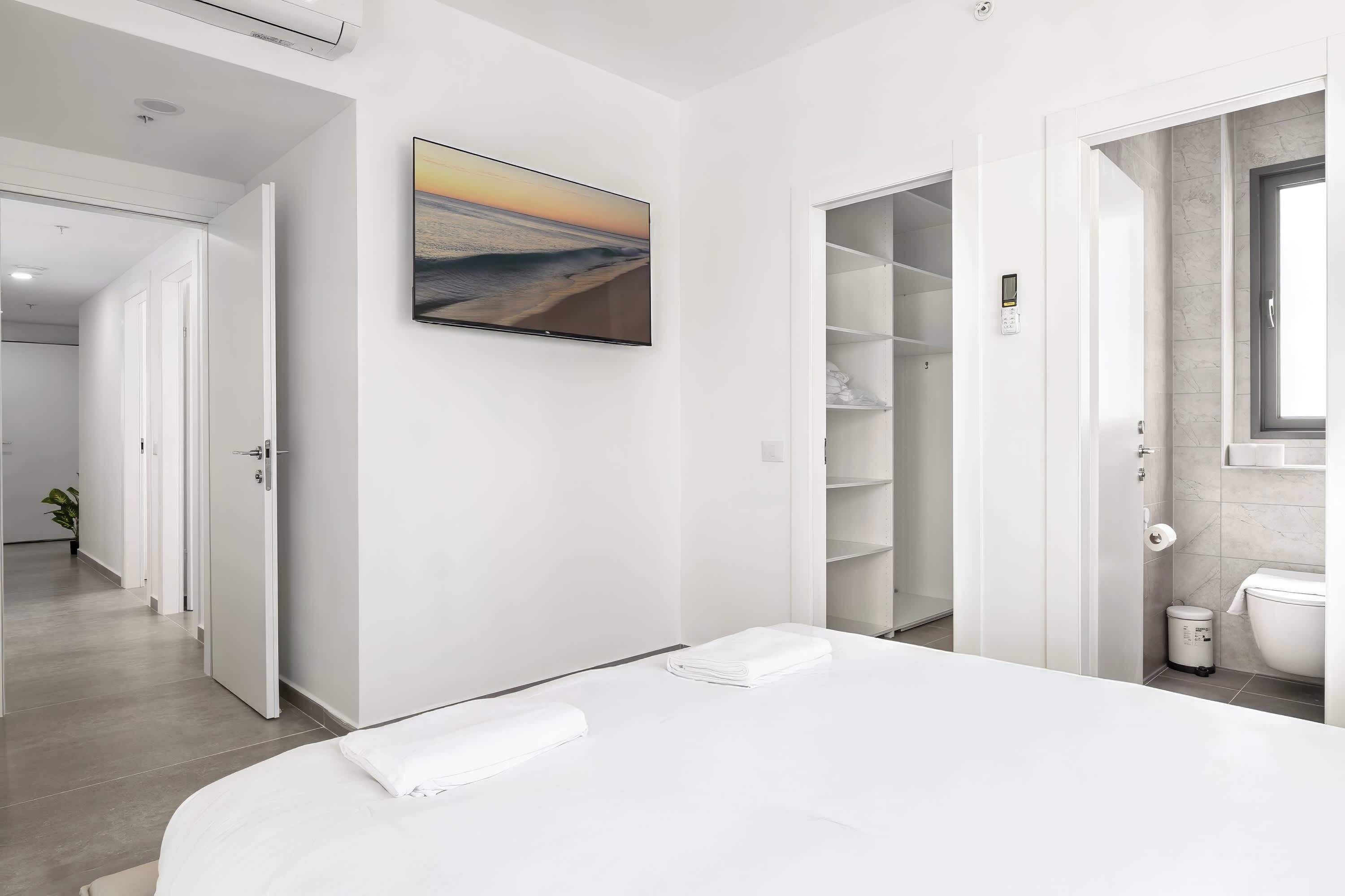 Ein modernes Hotelzimmer mit einem großen Bett, einem Sonnenuntergangsbild, einem begehbaren Kleiderschrank und einem Badezimmer mit Marmorwand.