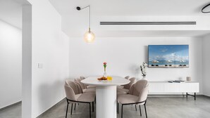 Een moderne eetruimte met een ronde tafel, zes stoelen, een hanglamp, een witte console tafel, en een groot gepresenteerd schilderij aan de muur.