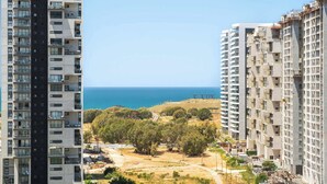 Een hoog appartementencomplex met meerdere balkons, een helder uitzicht op de zee en een glooiend landschap met bomen.