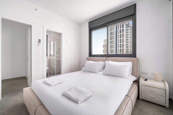 Een moderne hotelkamer met een groot bed, een nachtkastje, een raam met uitzicht op gebouwen en een deur naar een badkamer.