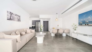 Een moderne woonkamer met een bank, salontafel, eethoek, keuken en kunstwerken aan de muren.