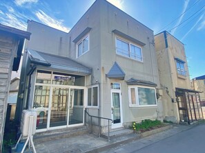 A two-story building with a ground-floor entrance, a small balcony, and a window with a metal railing. - TSUGARU HOUSE 2  A private villa rental in Aomori / Aomori City Aomori (Aomori City)