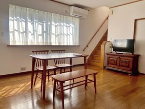 A dining area with a table and chairs, a bench, a TV on a cabinet, and a staircase. - TSUGARU HOUSE 2  A private villa rental in Aomori / Aomori City Aomori (Aomori City)