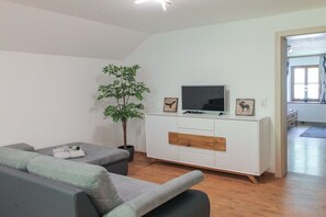 Ein modernes Wohnzimmer mit einem grauen Sofa, einer weißen Unterhaltungsanlage mit Flachbildfernseher, einer kleinen Pflanze und einem Holzschrank.
