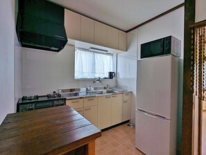Eine kleine Küche mit Holztisch, Herd, Kühlschrank und einem Fenster mit Vorhängen.