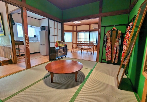 A traditional Japanese room with tatami flooring, a wooden table, and a view of a kitchen and dining area.
