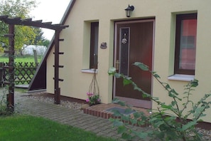 Ein Haus mit einer Holzpergola, einer Haustür und einem kleinen Vorbereich.