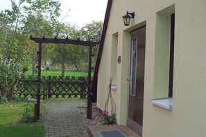 Ein Gebäudeeingang mit einer Holzpergola, einem kleinen Fenster und einer Tür.