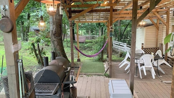 A covered outdoor area with a grill, white plastic chairs, and a hammock.