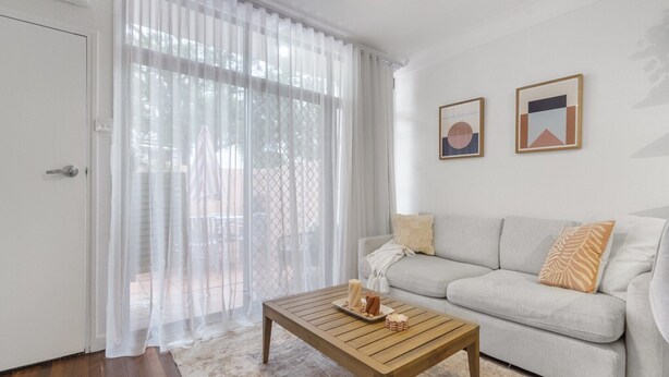 A living room with a sofa, a coffee table, and two framed pictures on the wall. - Courtyard 1-Bed Apartment in New Farm (New Farm)