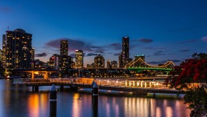 A city skyline at dusk with illuminated buildings, a bridge, and a calm river. - Courtyard 1-Bed Apartment in New Farm (New Farm)