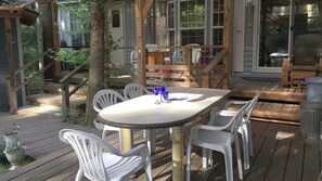 Ein Essbereich im Freien mit einem runden Tisch und weißen Stühlen, umgeben von einer Holzterrasse und einer überdachten Veranda.