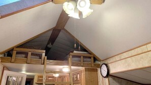 Una habitación con techo inclinado, vigas de madera, un reloj y una lámpara en el techo.