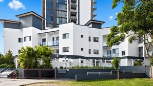 En modern flervåningsbyggnad med bostäder, balkonger, en grind vid entrén och en välskött gräsmatta.