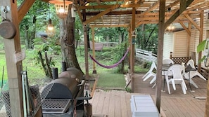 A covered outdoor area with a grill, white plastic chairs, and a hammock.
