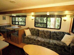 Un intérieur de camping-car accueillant, avec un canapé, une table et deux fenêtres donnant sur le paysage extérieur.