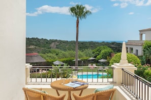 A balcony with wicker furniture, a view of a swimming pool, and lush greenery. - Charming Andalusian style Cortijo in La Reserva de Sotogrande (AN)