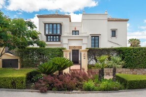 A two-story house with a front entrance, a balcony, and a garden with various plants. - Charming Andalusian style Cortijo in La Reserva de Sotogrande (AN)