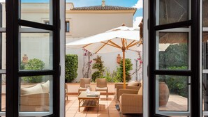 Eine offene Terrasse mit Korbmöbeln, einem weißen Sonnenschirm und Topfpflanzen.