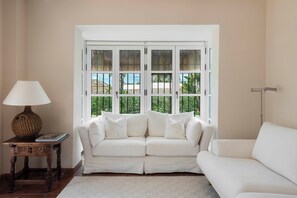 A white sofa, a lamp, and a window with a view of greenery. - Charming Andalusian style Cortijo in La Reserva de Sotogrande (AN)