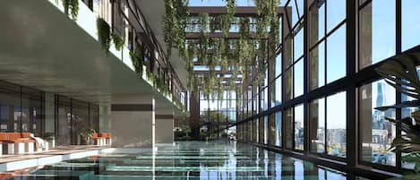 A modern indoor pool with glass walls, greenery, and a city view.