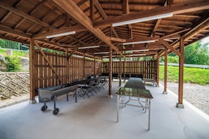 Une terrasse extérieure couverte, avec une longue table et des chaises, un barbecue et une clôture en bois.