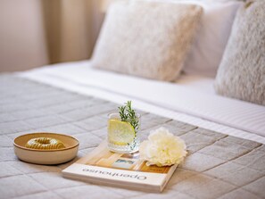 Uma cama com cobertura acolchoada, uma tigela, um copo com fatia de limão e alecrim, e um livro intitulado 'Pensionhouse'.