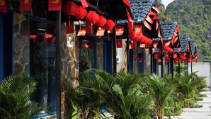 Una hilera de edificios de estilo tradicional con banderas rojas y farolillos, rodeada de abundante vegetación.