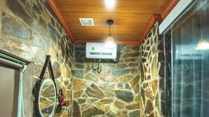 Un baño con pared de piedra, techo de madera, inodoro, lavabo con espejo y zona de ducha.