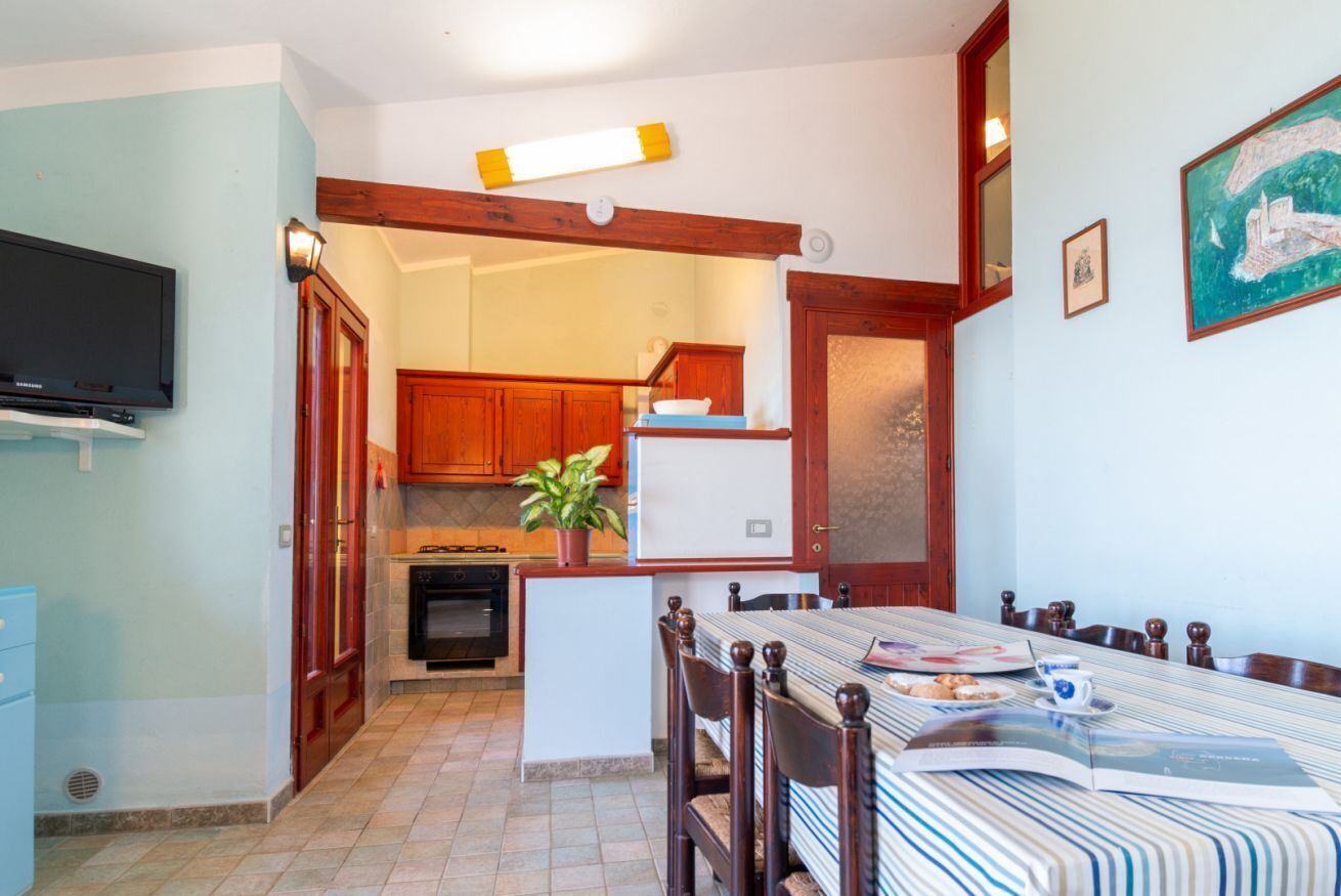 Un coin repas avec une nappe à rayures, des chaises en bois et un téléviseur fixé au mur.