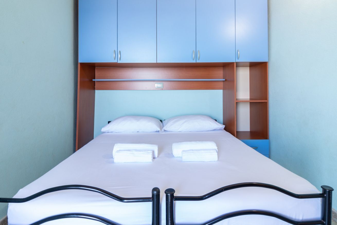 A single bed with a headboard, a wooden shelf below, and a light blue wall.
